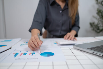 A woman is sitting at a desk with a laptop and a stack of papers