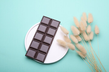 Dark chocolate bar on tray with lagurus floers,  blue background