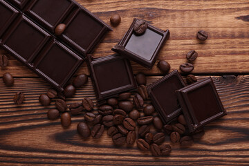 Blocks of broken chocolate bar with coffee beans on wooden background