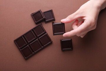 Hand holding Blocks of broken chocolate bar on brown background