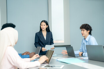 Fototapeta premium Asian businesswoman delivering a strategic presentation with charts to colleagues in a modern corporate office environment.