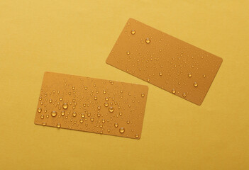 Golden business cards with water drops on yellow background