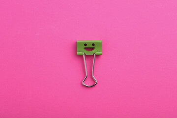 Binder clip with a smiling face on a pink background
