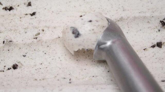 Close-up of a metal ice cream scooper holding a perfect ball of cookies and cream ice cream, surrounded by creamy textured ice cream with chocolate cookie bits.