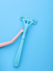 Dolls hand holding plastic razor on blue background