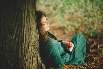 Woman in Green Resting Beneath a Tree with Apple