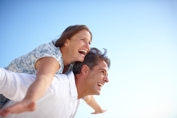 Fototapeta premium Piggyback, embrace and couple with smile, outdoor and holiday for romance, date and happy in relationship. Freedom, man and woman on vacation, bonding and commitment in marriage, mockup and travel