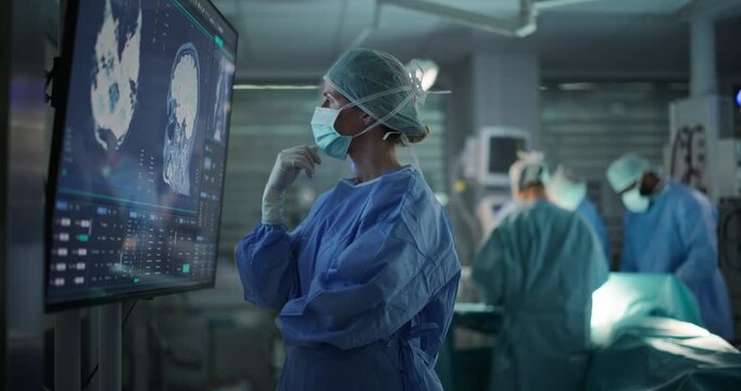 Professional Focused Caucasian Female Surgeon Reviewing Patient's Brain Scans on a Large Monitor, Preparing to Lead Her Team in a Complex Surgery, Analyzing Data Before the Procedure Begins