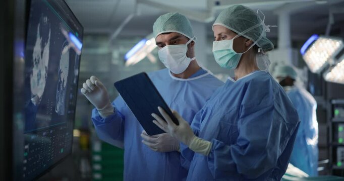 Before Beginning the Surgery, Female Lead Surgeon and an Assistant Looking at Detailed Brain Scans on a Large Computer Screen and a Tablet, Making Key Decisions Together with the Team