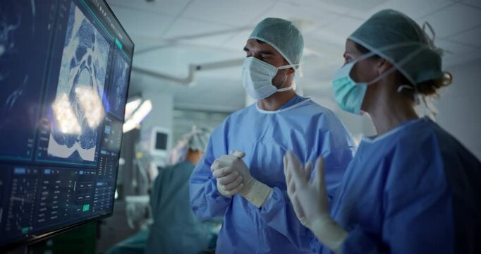 Caucasian Male and Female Surgeons Analyze Scans on a Digital Monitor, Planning Surgical Strategy in a High-tech Operating Room. Colleagues Working Together, Preparing for Surgery