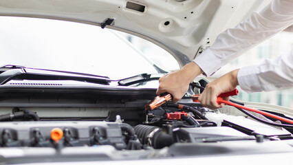 mechanic from the service center is helping to jump start the car battery for customer who has a deteriorated battery and cannot start the car. Jump starting the battery helps to continue the journey