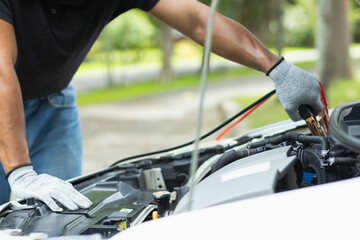 mechanic from the service center is helping to jump start the car battery for customer who has a deteriorated battery and cannot start the car. Jump starting the battery helps to continue the journey