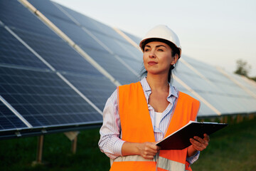 Checking the data, with notepad. Female worker engineer in uniform is near solar panels