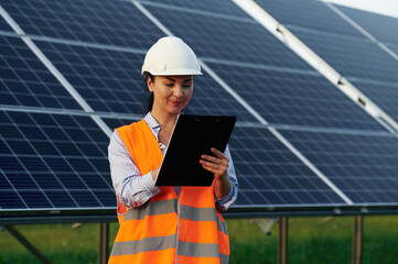 Notepad in hands. Female worker engineer in uniform is near solar panels