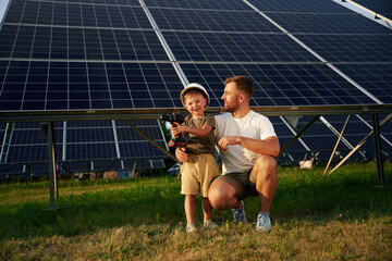 Posing with drill in hands. Father with his little son are together near the solar panels