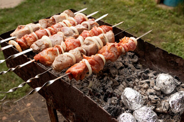 Juicy, appetizing barbecue on the grill. There are baked potatoes in foil next to it. Barbecue food, proper nutrition, outdoor food, fast food.