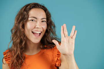 Portrait of young woman doing Vulcan salute with her hands. Woman isolated on blue background.