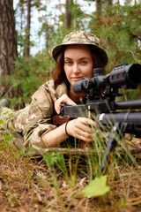 Fototapeta premium A focused female soldier lying in the forest, aiming with a sniper rifle during a training exercise in a natural setting