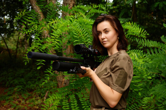 A woman stands confidently in a lush green forest, holding a hunting rifle with a scope, showcasing her skill and focus during an outdoor training session in broad daylight