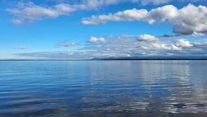 Obraz premium The blue lake merges on the horizon with the sky and white clouds