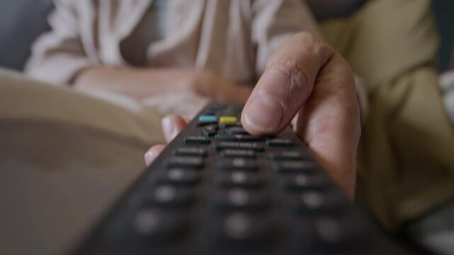 Closeup of unrecognizable woman holding remote control and pressing buttons, switching channels while watching TV at home