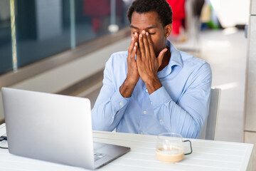 Frustrated man covering face while sitting in front of laptop