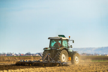 Fototapeta premium A tractor with plow in action, turning over the soil on a sunny day