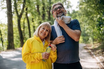 Holding bottle of water, after sport exercises. Senior couple together outdoors at nature