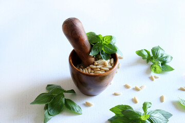 Mortaio di legno con pinoli e foglie di basilico fresco su fondo di legno bianco. Direttamente sopra.