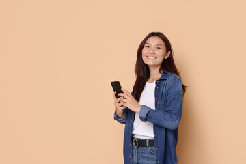 Smiling woman with smartphone on beige background. Space for text