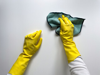 Hands in a yellow rubber gloves for cleaning and household chores holding a green cleaning cloth. Hands in protective gloves on a white background.