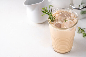 Glass of iced scented aromatic rosemary coffee latte, with whipped milk or cream, cold coffee drink decorated with sprig of rosemary