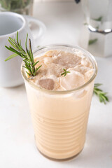Glass of iced scented aromatic rosemary coffee latte, with whipped milk or cream, cold coffee drink decorated with sprig of rosemary