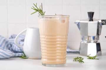 Glass of iced scented aromatic rosemary coffee latte, with whipped milk or cream, cold coffee drink decorated with sprig of rosemary