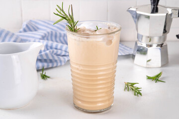 Glass of iced scented aromatic rosemary coffee latte, with whipped milk or cream, cold coffee drink decorated with sprig of rosemary