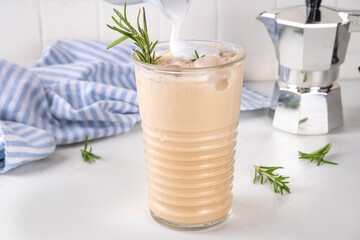 Glass of iced scented aromatic rosemary coffee latte, with whipped milk or cream, cold coffee drink decorated with sprig of rosemary