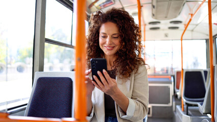 Beautiful, mid adult woman using smartphone while riding in a city bus