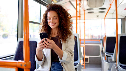 Beautiful, mid adult woman using smartphone while riding in a city bus