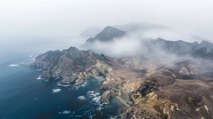 Fototapeta premium An aerial view of a rugged coastline with fog rolling in over the mountains.