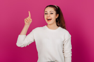 Joyful Young Woman Pointing Upward with a happy Smile. Standing against a bright colorful background