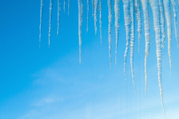 Obraz premium Frozen icicles on the roof on the background of the blue sky, natural long icicles, winter background