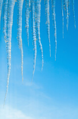 Winter background with long frozen icicles on the roof on the background of the blue sky, natural long icicles, winter nature background
