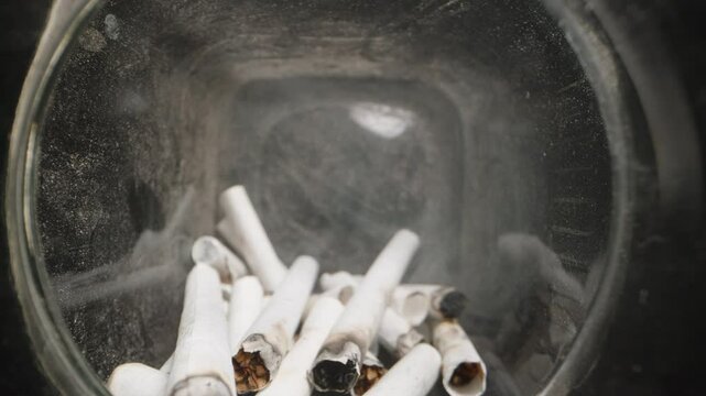 Dolly slider, close up. Close-up view inside a glass jar filled with cigarette butts, highlighting the health risks and environmental impact of smoking, with visible ashes and burnt filters in a confi