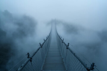Fototapeta premium Misty suspension bridge stretches into foggy landscape at dawn