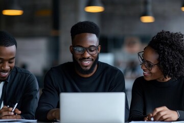 Obraz premium A group of three people collaborates happily in a modern office setting, focused on a laptop, symbolizing teamwork and professional camaraderie.
