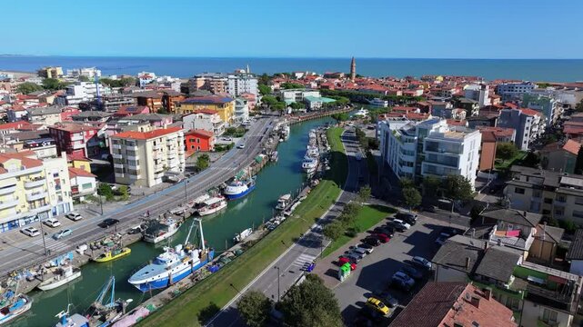 aerial toward the Adriatic Sea following the canal in Caorle, Italy north of Venice. Commercial fishing boats are anchored in the bustling city center