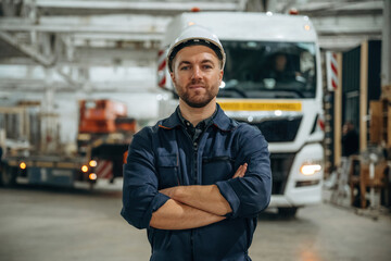 Standing in front of a truck. Male worker is in the modern warehouse or manufacturing company