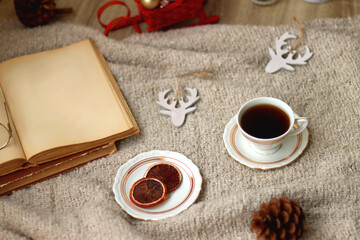 Various Christmas decorations, lit candles, cup of tea or coffee, cookies, books, presents and soft blanket on the table. Holiday hygge at home. Selective focus.