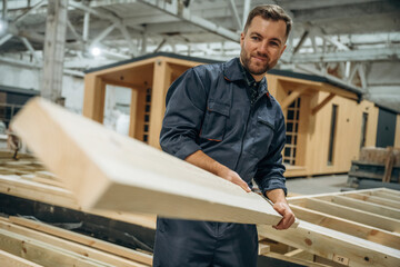 The plank, man is holding it. Male builder is at construction of wooden house