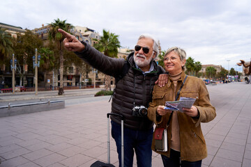 Happy Caucasian senior couple doing tourism using a travel map to locate on the city, enjoying...